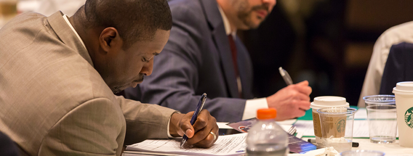 2 men writing in notebooks during symposium