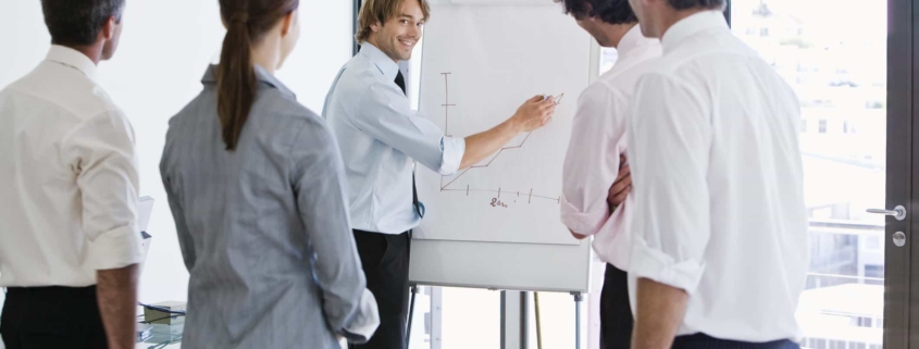 Four employees watching their manager draw a graph