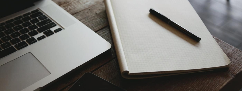 Notepad, laptop, and pen on desk