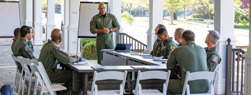 Fighter pilot team gathered around mission planning table, led by a facilitator – boosting leadership performance through high-pressure collaboration.